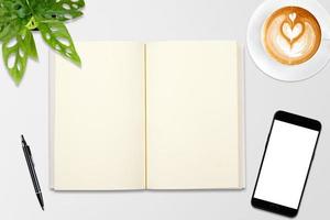 An open blank notebook, smartphone with pen and a cup of latte coffee on wooden table. photo