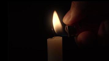 närbild av en hand som tänder ett vitt ljus med en tändare i ett mörkt rum. video