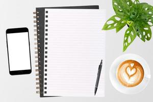 un cuaderno en blanco abierto, un teléfono inteligente con bolígrafo y una taza de café con leche en una mesa de madera. foto