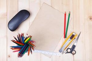 Workplace with colored pencils and supplies, paper, eyeglass on wooden table photo