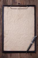 Old blank paper on clipboard with space on wood background photo