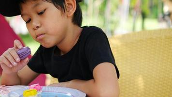 menino de 7 anos comendo macaron em restaurante ao ar livre video