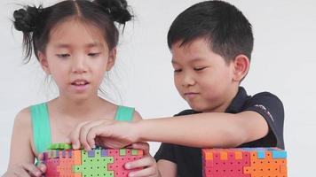 les enfants asiatiques jouent à un jeu créatif de bloc de puzzle en plastique pour pratiquer leurs compétences physiques et mentales video