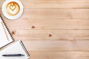 An open blank notebook with pencil and a cup of coffee on wooden table. Latte art coffee on top photo