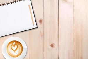 An open blank notebook with pencil and a cup of coffee on wooden table. Latte art coffee on top photo