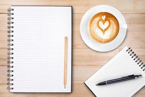An open blank notebook with pencil and a cup of coffee on wooden table. Latte art coffee on top photo