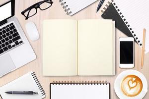 cuaderno abierto en blanco con bolígrafo, gafas y teléfono móvil, taza de café con leche en la mesa de madera. maqueta de plantilla comercial para agregar su texto. vista superior. foto