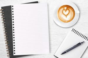 An open blank notebook with pencil and a cup of coffee on wooden table. Latte art coffee on top photo