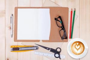 un cuaderno en blanco abierto con lápices de colores, bolígrafos y una taza de café sobre una mesa de madera foto