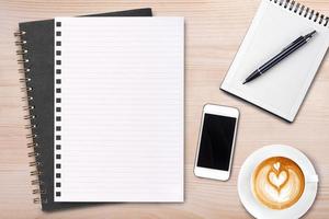 An open blank notebook with pen and a cup of coffee on wooden table. Latte art coffee on top photo