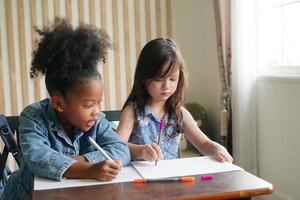 Preschool Girl Kid Drawing With Color Pencil On White Paper On Table In Classroom With Friends photo