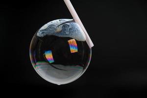 Beautiful soap bubbles are blown with a straw on a black background. Abstract soap bubbles with colorful reflections.