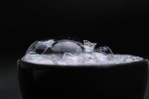 Black cup with foam water and bubbles on black background. Soap bubbles in motion background. photo