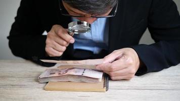 Business man is checking genuine Thai Banknote using magnifier