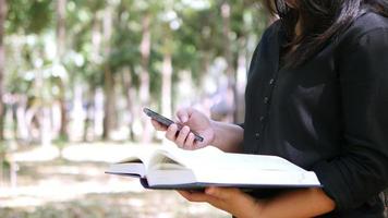 Lady using mobile phone while reading book in the park video