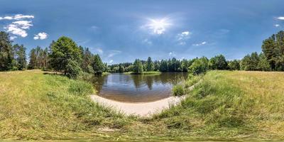 panorama hdri esférico sin inconvenientes vista en ángulo de 360 grados en la costa de hierba de un pequeño lago o río en un día soleado de verano y clima ventoso con hermosas nubes en proyección equirectangular, contenido vr foto