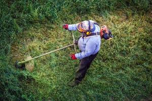 Top view fat dirty lawnmover man worker cutting dry grass with lawn mower. photo