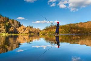 niño pescador en un paisaje panorámico con un río ancho y ancho en el bosque de otoño en un día soleado con reflejo foto