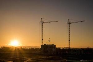 grúas torre de silueta y edificios altos de varios pisos sin terminar en construcción al atardecer en el desierto en un sitio de construcción iluminado foto