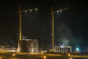 grúas de torre y altura de varios pisos sin terminar cerca de edificios en construcción en el fondo nocturno foto