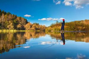 Fisherman boy on panoramic landscape with wide broad river in autumn forest in sunny day with reflection photo