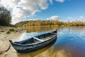 old wooden boat on the bank of a wide river in sunny day photo