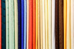 wide selection of different color textile silk fabrics clothes lay in row in drapery store photo