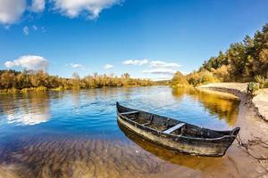 old wooden boat on the bank of a wide river in sunny day photo