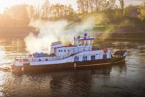 a small steamer ship on wide river in the rays of the setting sun photo