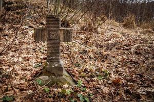 Old tombstone cross of the First World War overgrown with moss and old leaves in the autumn forest photo