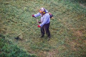 Top view fat dirty lawnmover man worker cutting dry grass with lawn mower. photo