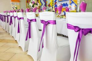 hermosas flores en la elegante mesa de la cena en el día de la boda. decoraciones servidas en la mesa festiva con fondo violeta foto