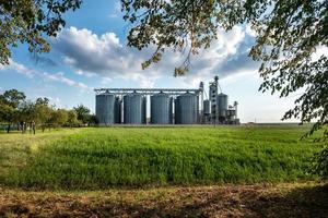 silos de plata en plantas agroindustriales para el procesamiento, secado, limpieza y almacenamiento de productos agrícolas, harina, cereales y granos con hermosas nubes foto