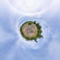 tiny planet in blue sky with sun and beautiful clouds. Transformation of spherical panorama 360 degrees. Spherical abstract aerial view. Curvature of space. photo