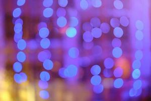 Blurred bokeh colorful lights lanterns, holiday new year lighting on black background Christmas winter glitter shiny light bokeh in rainbow colors. Holiday purple blue pink violet natural texture. photo