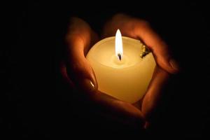 burning candle in the hands of a praying girl on a black background photo
