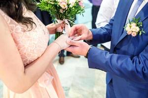 el novio abraza a la novia con ramo de novia con rosa violeta. el novio viste un anillo de compromiso a la novia. recién casados intercambian anillos de boda foto