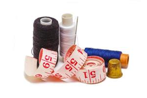 Needle, spools of thread, measuring tape and thimble as symbols for tailoring isolated on white background photo