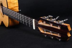 Tuning pegs on wooden machine head of six strings acoustic guitar neck on black background photo