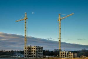 grúas torre de silueta y edificios altos de varios pisos sin terminar en construcción en un día nublado con luna foto