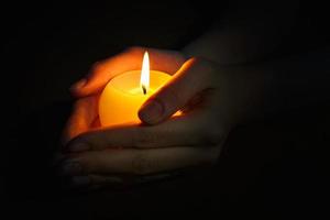 burning candle in the hands of a praying girl on a black background photo