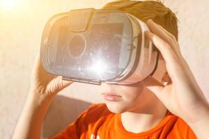 boy in orange t-shirt with VR AR 360 virtual reality glasses cardboard for mobile phone playing the game. Device for watching movies for travel and entertainment in 3d space. photo