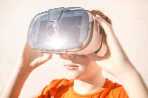 boy in orange t-shirt with VR AR 360 virtual reality glasses cardboard for mobile phone playing the game. Device for watching movies for travel and entertainment in 3d space. photo