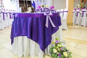 hermosas flores en la elegante mesa de la cena en el día de la boda. decoraciones servidas en la mesa festiva con fondo violeta foto