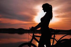 Summer silhouette landscape. Girl with a bicycle by the lake against the backdrop of the setting sun, the crimson sunset photo