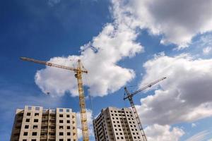 Tower cranes and unfinished multi-storey high near buildings under construction site in the sunny day with beautiful clouds photo