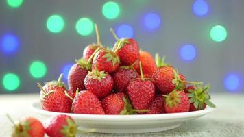 Strawberry stack in white dish over colorful blink light bokeh background video
