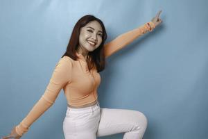 retrato de una joven y hermosa mujer asiática de pie y sonriendo a la cámara, aislada de fondo azul foto