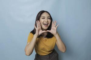 Surprised Asian woman reclines on her hands and shouting while looking at the camera over blue background photo