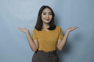 An excited young woman presenting and pointing copy space on her side, isolated on blue background photo